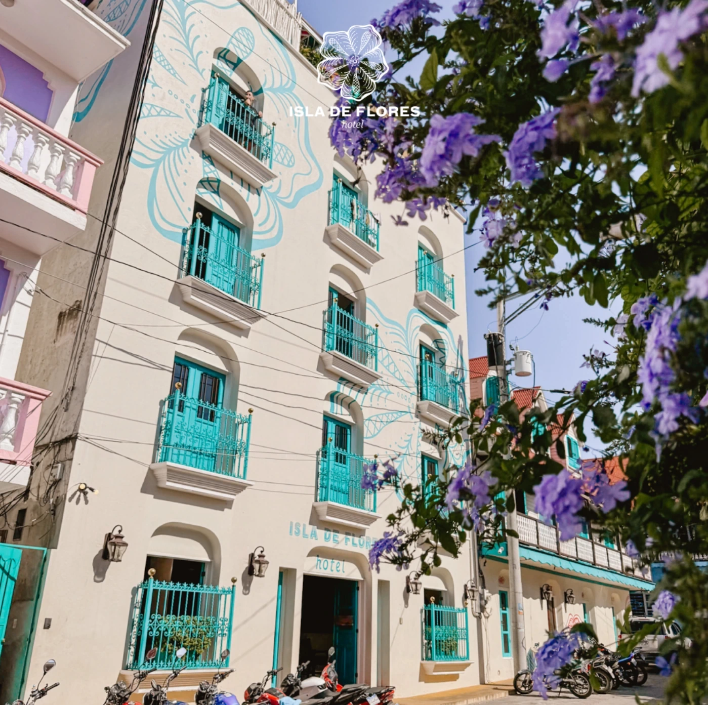 Fachada colonial del hotel con balcones turquesa y jacarandas