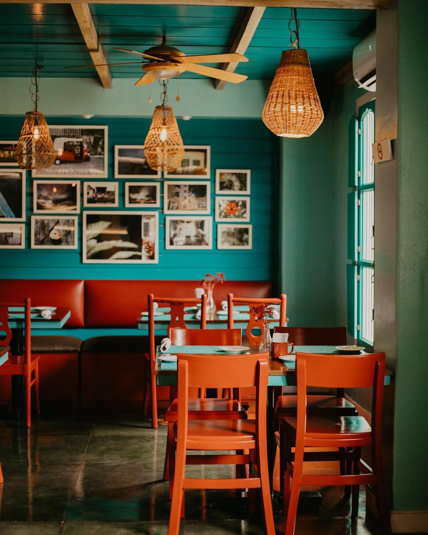 Restaurante con paredes turquesa, sillas naranjas y lámparas de mimbre